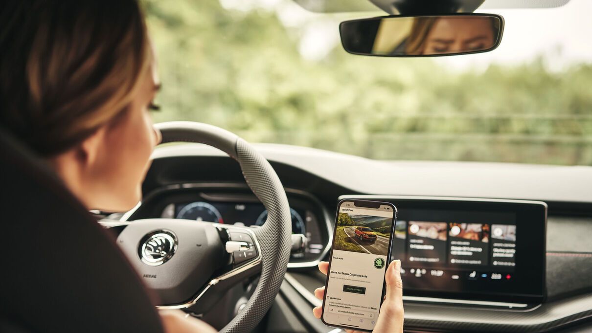 A lady holding her phone showing Skoda website of the MySkoda app