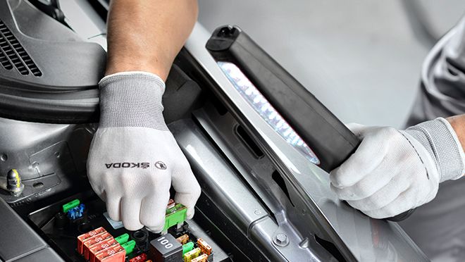 Close up view of a technician hand wearing a Škoda glove, removing a cartridge from the car engine